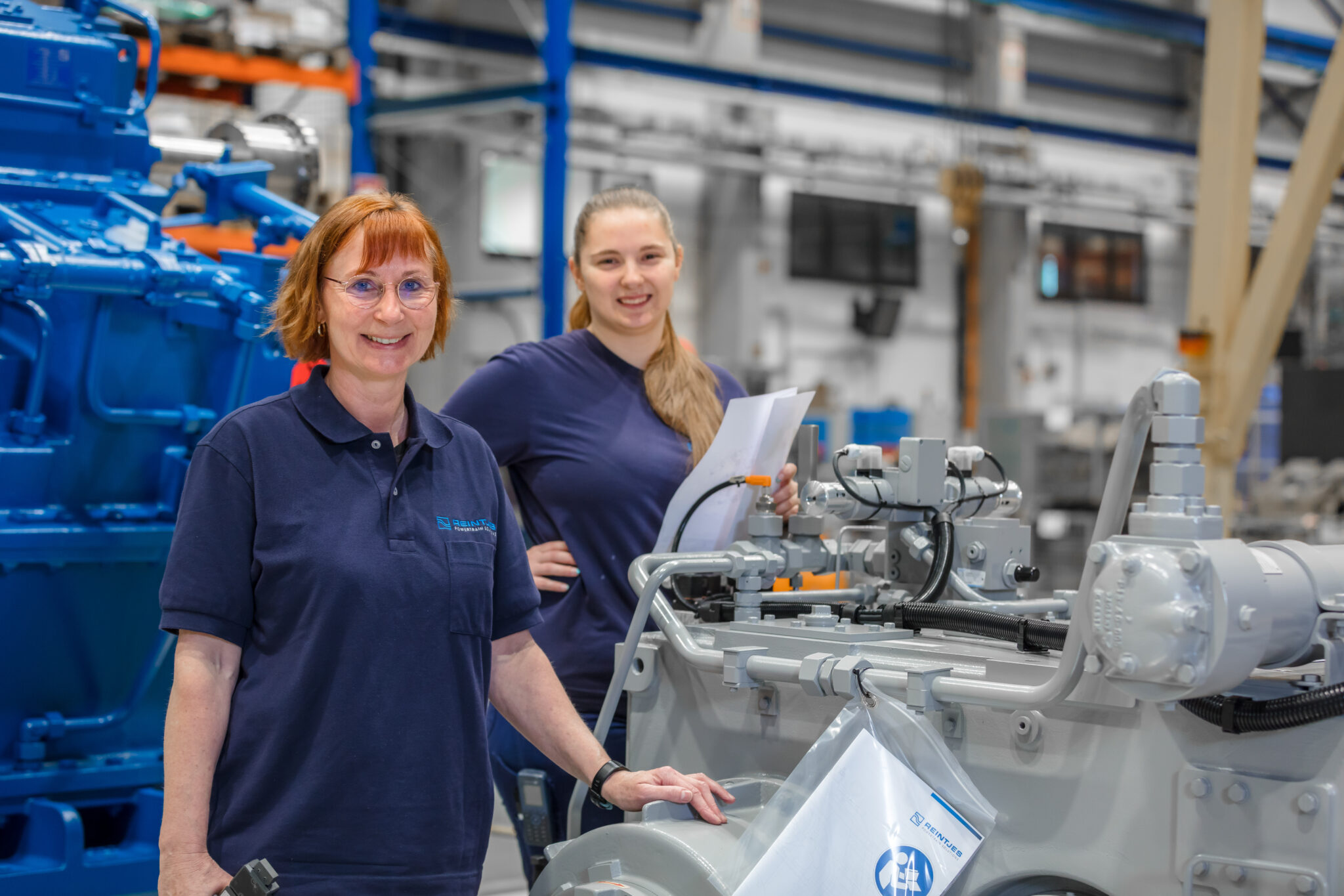 Zwei REINTJES Mitarbeiterinnen stehen in einer der Produktionshallen in Hameln zwischen Getrieben.